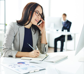 Busy secretary talking on mobile phone while making notes and looking at monitor